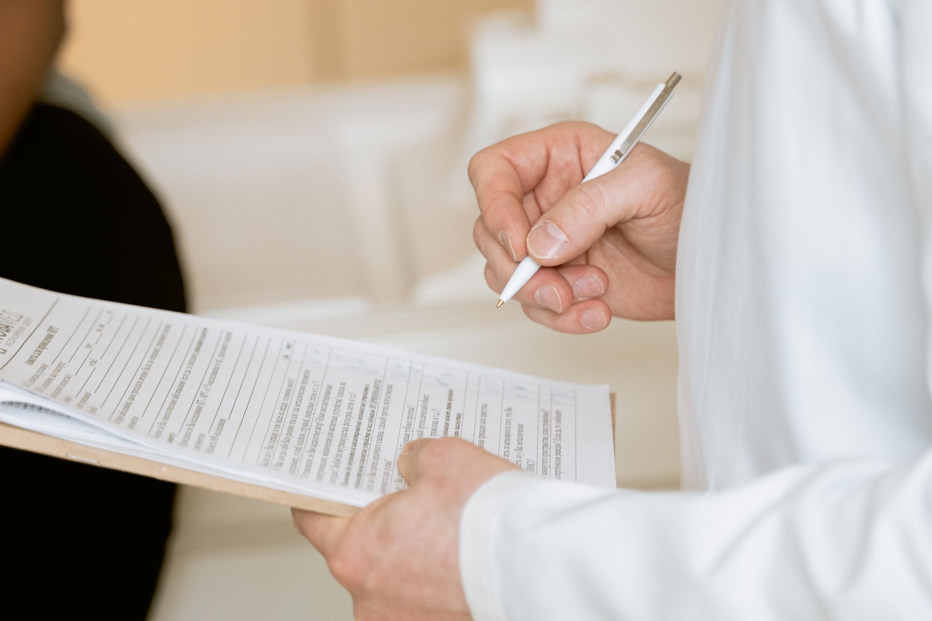 A hand writing clinical notes on a clipboard