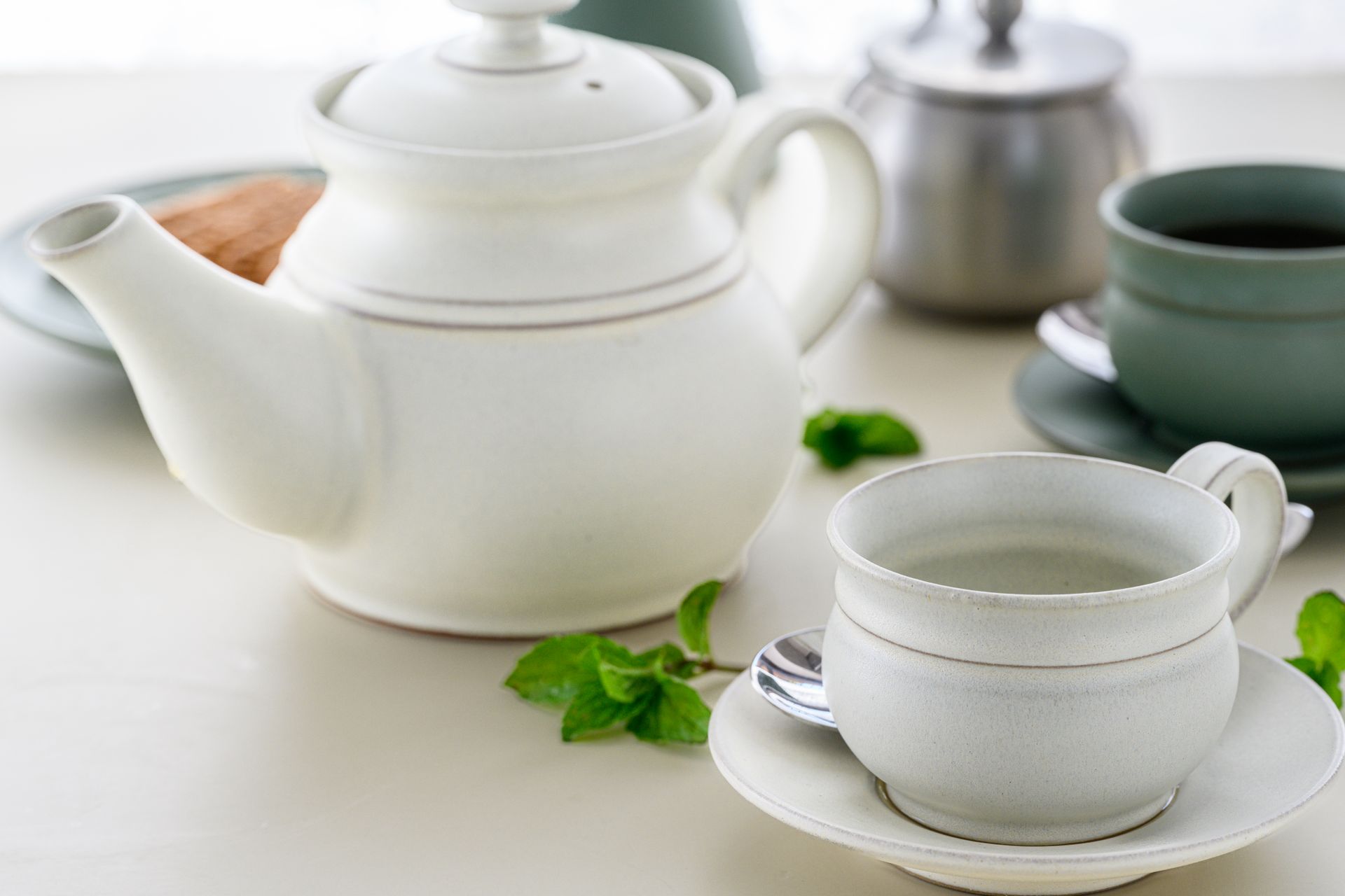 A white teapot and cup with mint